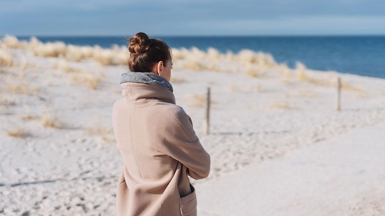 Frau blickt gedankenverloren auf das Meer hinaus; Behandlung von Stressfolgeerkrankungen wie der Depression in der Blomenburg Privatklinik In der Blomenburg Privatklinik behandeln wir Stressfolgeerkrankungen wie die Depression ganzheitlich und nachhaltig.