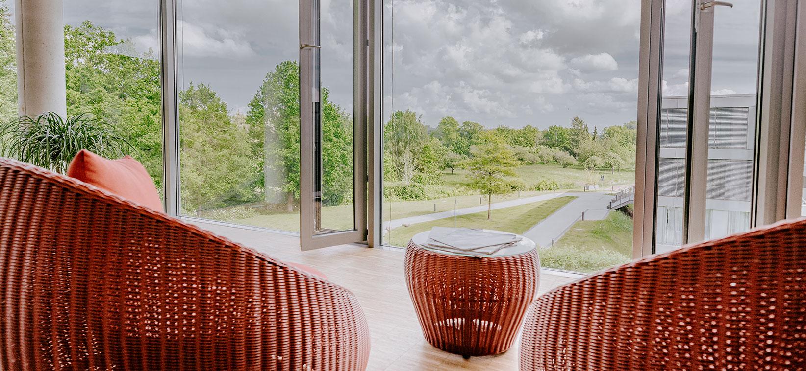 Grüner weitläufiger Ausblick aus dem Wintergarten im Loungebereich der Blomenburg Privatklinik Rückzugsorte mit grünem Ausblick in der Blomenburg Privatklinik laden zum Entspannen ein.