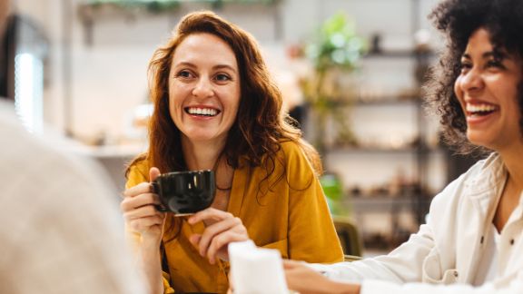 Junge Frau lacht gemeinsam mit Freunden in einem Cafe