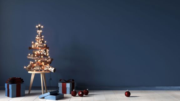 Weihnachtsbaum aus Holzscheiten vor blauer Wand mit Geschenken