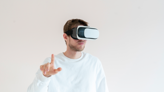 Junger Mann trägt VR-Brille und deutet in die Luft bei der Therapie