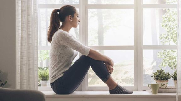 Junges Mädchen sitzt nachdenklich auf der Fensterbank und schaut aus dem Fenster Das Fachzentrum Falkenried biete eine spezialisierte Kinder- und Jugendlichenpsychotherapie in Hamburg-Eppendorf an.