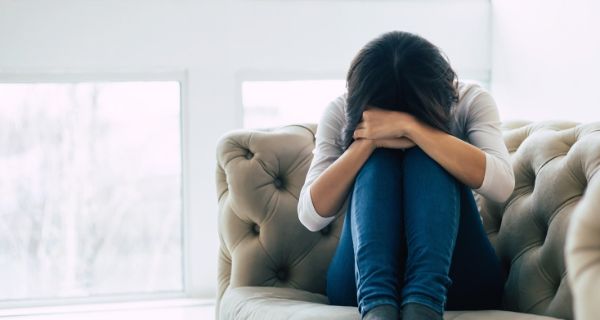 Frau leidet unter der Generalisierten Angststörung und sitzt zusammengekrümmt auf der Couch Die Blomenburg Privatklinik klärt über die Generalisierte Angststörung auf.