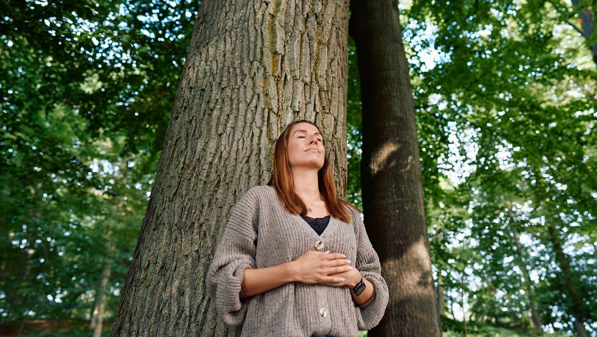 Patientin lehnt am Baum und atmet tief durch