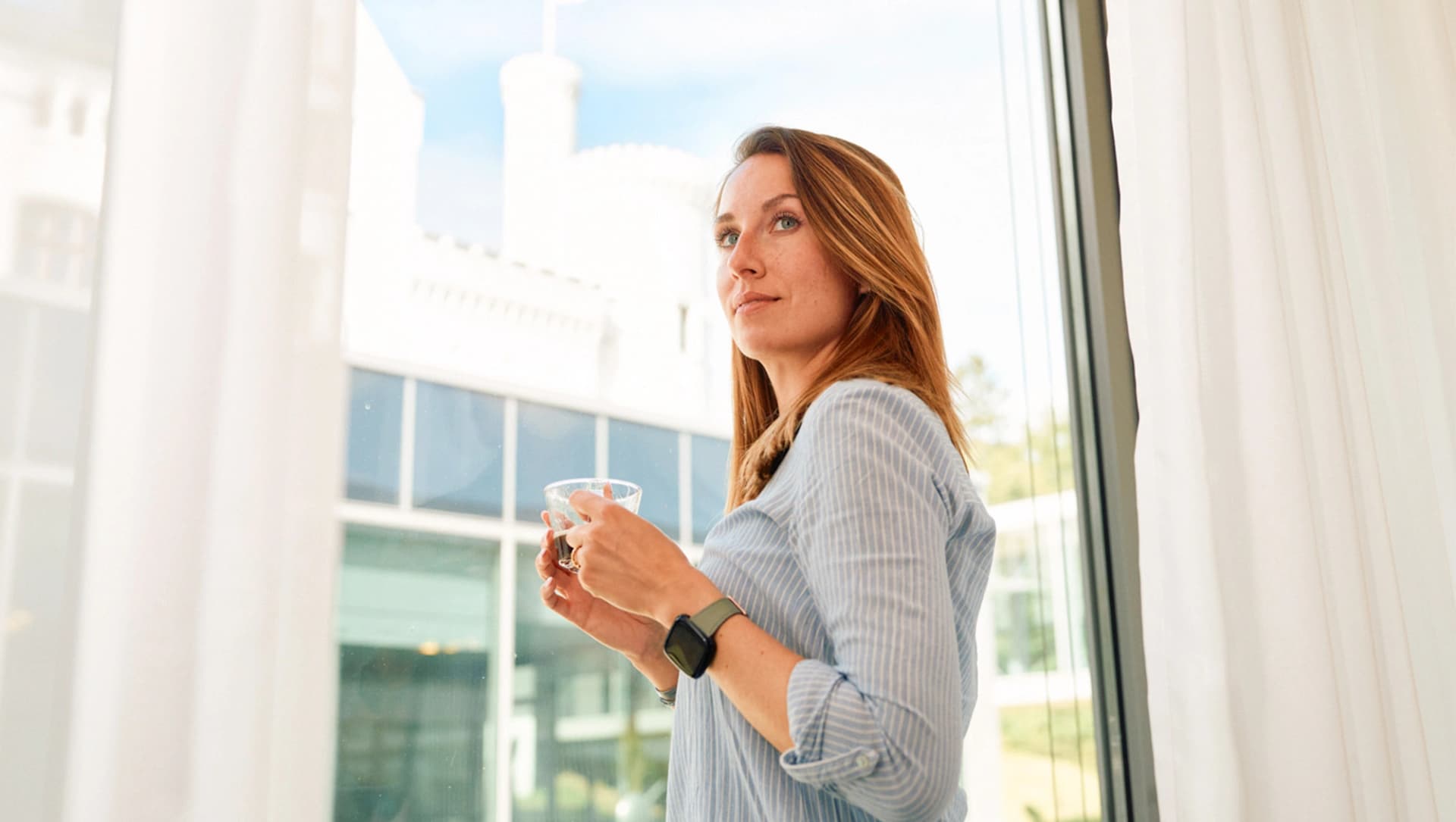 Patientin steht mit Kaffee vor dem Fenster in einem Patientenzimmer